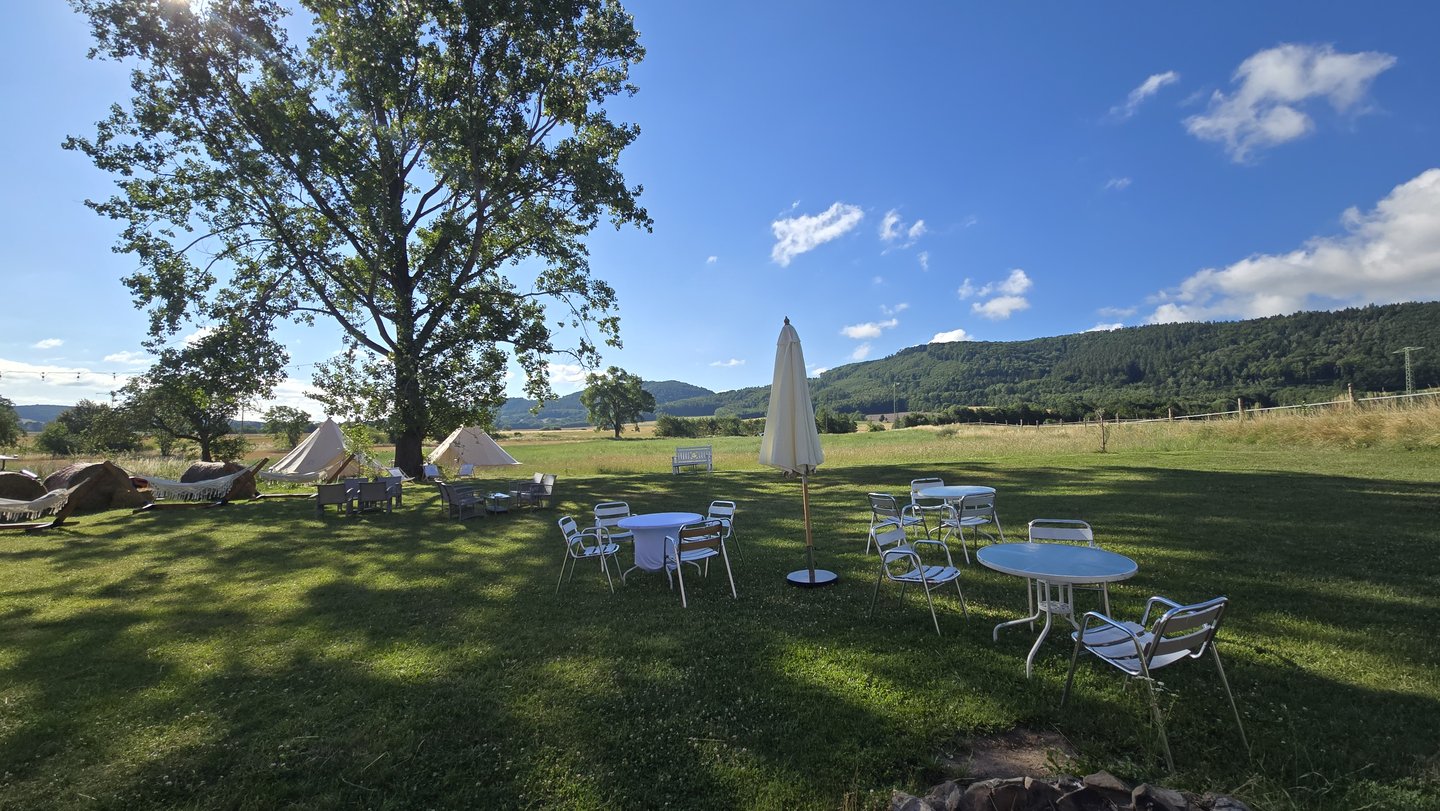 Łąka: duże drzewo, stoliki, parasol, glamping w tle, wzgórza