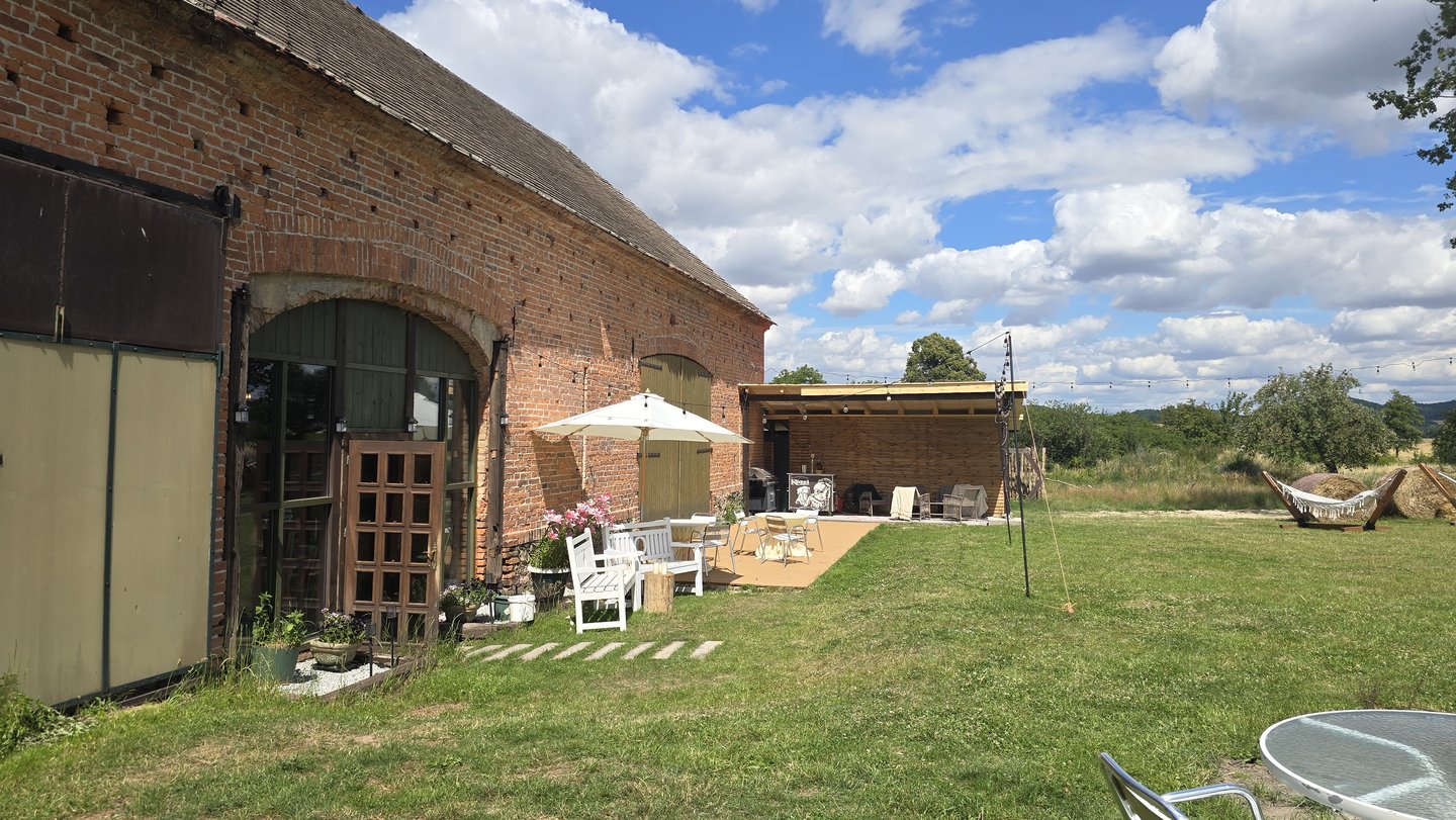 Fasada stodoły z otwartą bramą, parasol, leżak, wiata