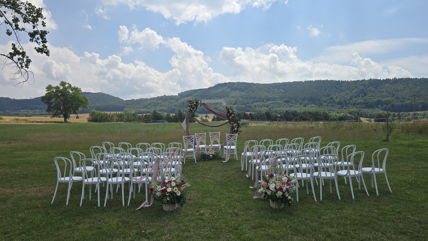 Ceremonia bez ludzi: białe krzesła, łuk kwiatowy, wzgórza, słońce