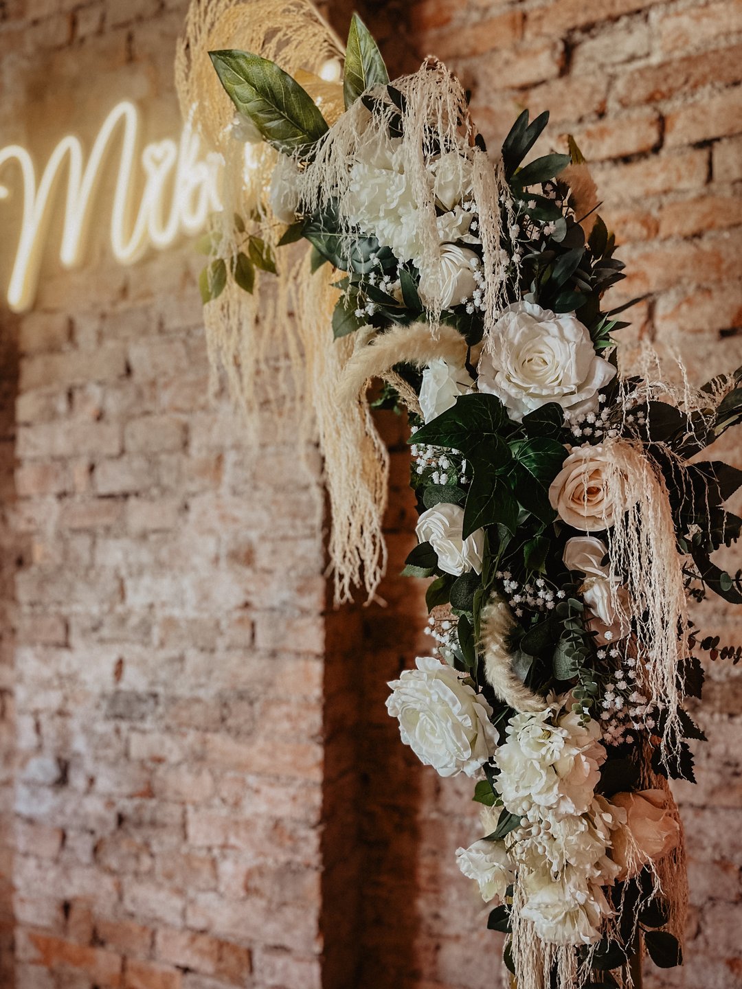 Pionowe: neon „Miłość” i białe kwiaty na cegle, zbliżenie