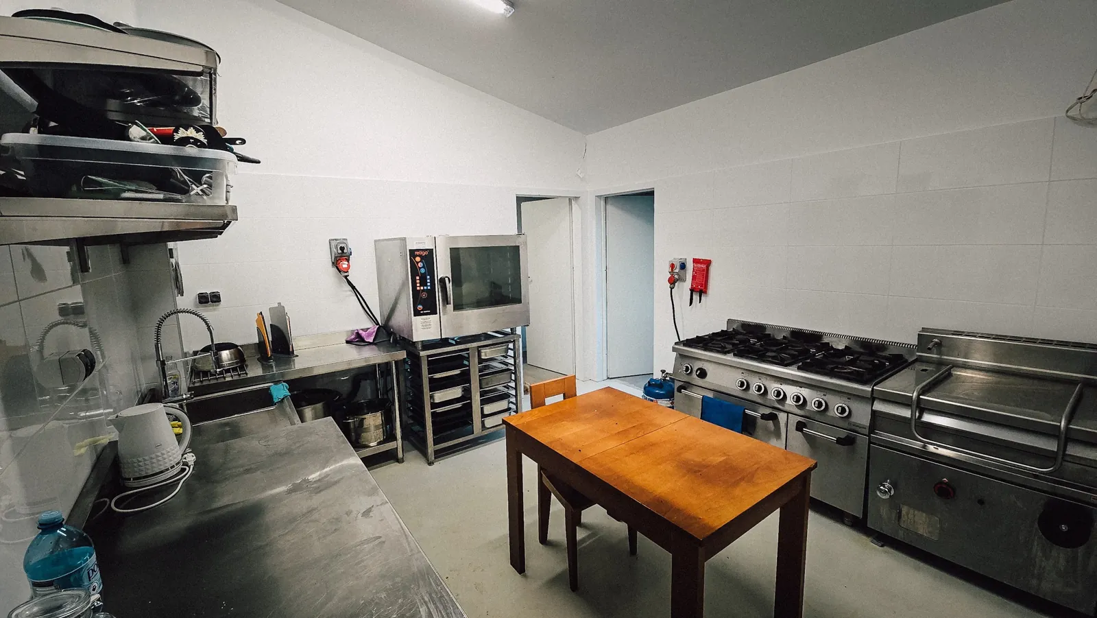 Catering back-of-house: a convection oven on a GN rack stand, a six-burner gas range, a braising pan and a wooden table