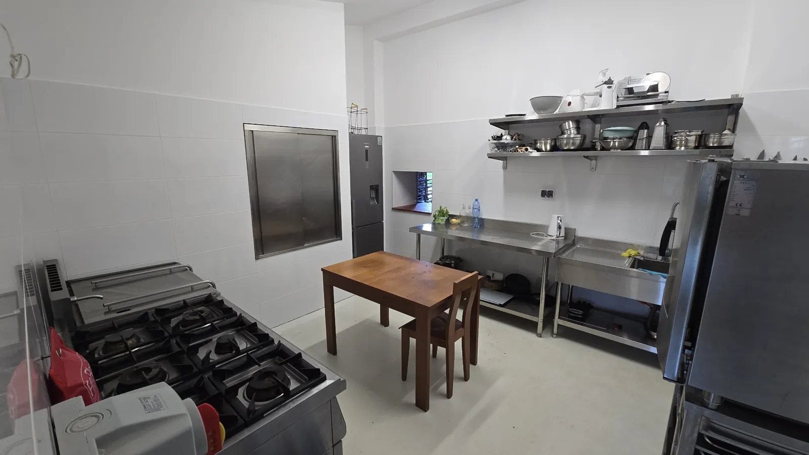Six-burner gas range, fridge, stainless-steel tables and sink, shelves of pots